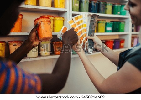 Cropped picture of multicultural graphic technology female workers' hands holding paint bucket and color swatch in printing workshop. Close up of silk screen printers choosing paint buckets for print.