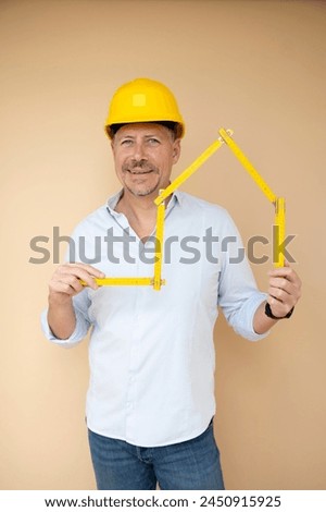 man, architect, technician, builder, polisher with yellow safety helmet and yellow folding rule against a brown background Royalty-Free Stock Photo #2450915925