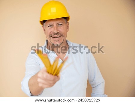 man, architect, technician, builder, polisher with yellow safety helmet and yellow folding rule against a brown background Royalty-Free Stock Photo #2450915929