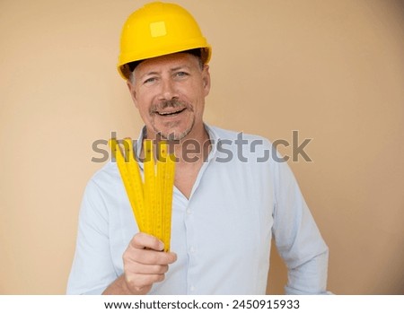 man, architect, technician, builder, polisher with yellow safety helmet and yellow folding rule against a brown background Royalty-Free Stock Photo #2450915933