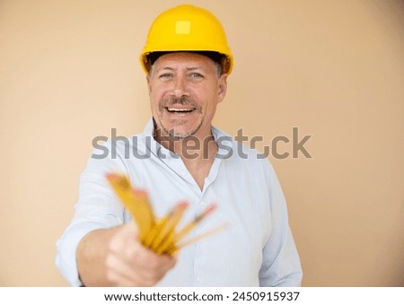 man, architect, technician, builder, polisher with yellow safety helmet and yellow folding rule against a brown background Royalty-Free Stock Photo #2450915937