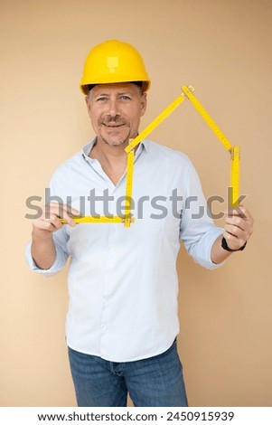 man, architect, technician, builder, polisher with yellow safety helmet and yellow folding rule against a brown background Royalty-Free Stock Photo #2450915939