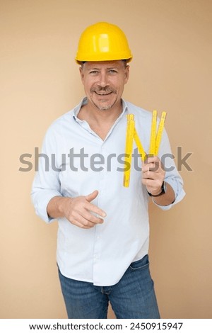 man, architect, technician, builder, polisher with yellow safety helmet and yellow folding rule against a brown background Royalty-Free Stock Photo #2450915947