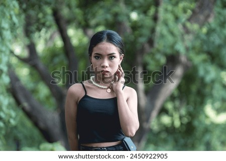 A striking photograph capturing a young woman styled in classic goth-inspired fashion, complemented by the natural beauty of a serene forest backdrop.
