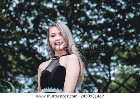 Elegant young woman wearing goth inspired clothing stands cheerfully in a lush forest setting, conveying a sense of style and subculture.