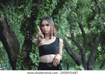 Young woman dressed in goth-inspired attire standing confidently in a lush, moody forest, pointing towards the camera.