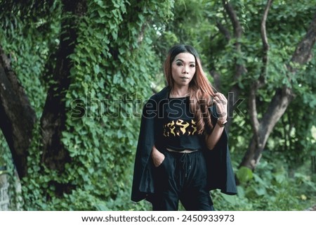 A young woman dressed in goth-inspired attire stands among verdant forest foliage, enhancing the mystical and serene ambiance.