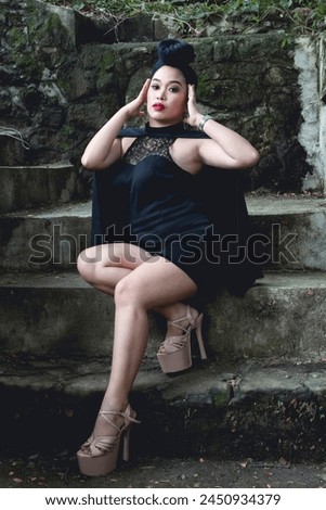 A stylish young woman wearing goth-inspired fashion sits elegantly on stone steps in a serene forest backdrop.