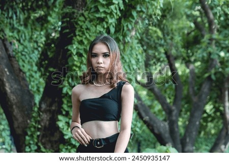 A young woman models a stylish gothic-inspired black outfit against a natural forest background, showcasing a bold and contemporary look.