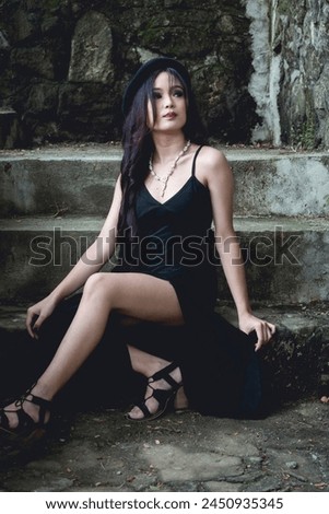 A portrait of a young woman dressed in gothic-inspired fashion, seated outdoors at the stairs of some ruins, exuding a mysterious aura.