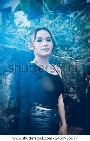 A young woman dressed in stylish goth-inspired clothing stands amidst a lush forest backdrop, exuding a sense of mystery and enchantment.