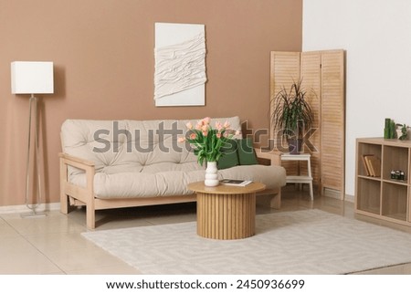 Interior of modern living room with sofa, chest of drawers, 3D textile artwork, table and vase with tulips