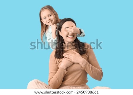 Cute little girl covering her mommy's eyes on blue background. Mother's Day celebration Royalty-Free Stock Photo #2450938661