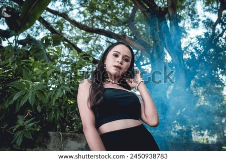 Elegant young woman dressed in goth-inspired fashion stands confidently in a lush forest background, exuding a mysterious and enchanting vibe.