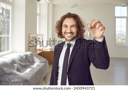 Portrait of a happy young bearded man with keys in his hands looking at the camera in new house and smiling . Real estate agent or joyful new homeowner enjoying real estate purchase. Royalty-Free Stock Photo #2450943721
