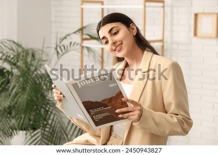 Beautiful young happy woman reading magazine at home