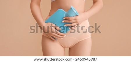 Young woman in menstrual panties and with hot water bottle on beige background, closeup