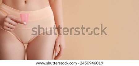Young woman in menstrual panties with and silicone cup on beige background with space for text