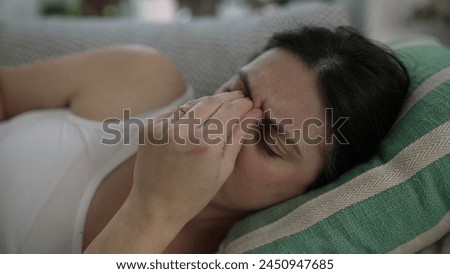 Stressed 30s woman close-up face laid on couch frowning putting hands in forehead struggles with life's challenges and headache Royalty-Free Stock Photo #2450947685