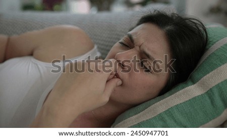 Stressed 30s woman close-up face laid on couch frowning putting hands in forehead struggles with life's challenges and headache Royalty-Free Stock Photo #2450947701