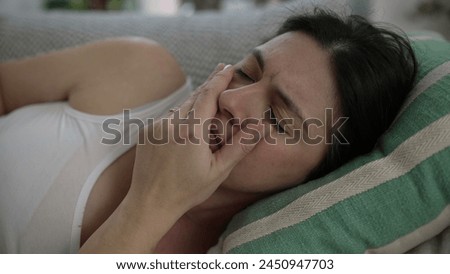 Stressed 30s woman close-up face laid on couch frowning putting hands in forehead struggles with life's challenges and headache Royalty-Free Stock Photo #2450947703