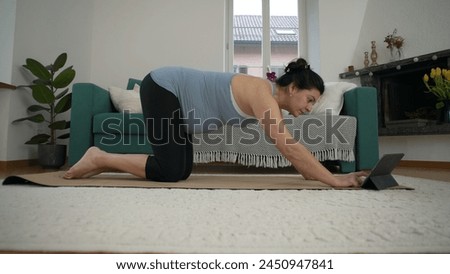 At-Home Yoga for Expectant Mothers - 30-Something Woman Focusing on Prenatal Poses in Living Room, Cultivating Wellness and Serenity in Late Pregnancy in front of tablet device guidance