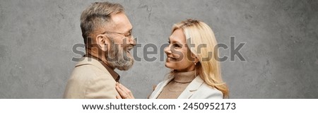 A mature, loving couple in debonair attire stand together on a gray backdrop. Royalty-Free Stock Photo #2450952173