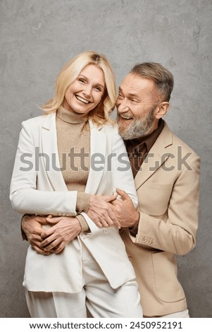 An elegant mature couple in debonair attires sharing a warm and tender embrace on a gray backdrop. Royalty-Free Stock Photo #2450952191