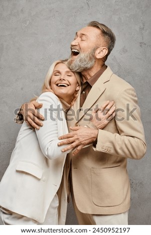 A mature, elegant couple dressed in debonair attires enveloped in a warm, loving embrace against a gray backdrop. Royalty-Free Stock Photo #2450952197