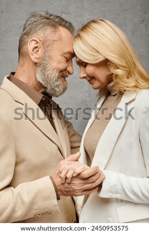 A mature loving couple in debonair attire holding hands and smiling on a gray backdrop. Royalty-Free Stock Photo #2450953575