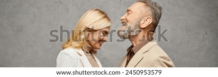 An elegant, mature loving couple in debonair attires pose together on a gray backdrop. Royalty-Free Stock Photo #2450953579