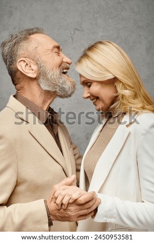 Elegant, mature, loving couple in debonair attires stand together against a gray backdrop. Royalty-Free Stock Photo #2450953581
