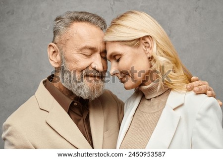Mature man and woman, dressed in debonair attires, embrace each other lovingly against a gray backdrop. Royalty-Free Stock Photo #2450953587