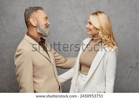 An elegant, mature man and woman stand side by side in debonair attire against a gray backdrop. Royalty-Free Stock Photo #2450953751