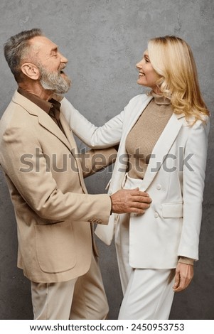 A mature man and woman in debonair attire stand side by side, exuding love and grace against a gray backdrop. Royalty-Free Stock Photo #2450953753