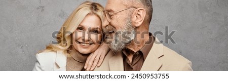 A mature, elegant couple in debonair attire posing gracefully against a gray backdrop.