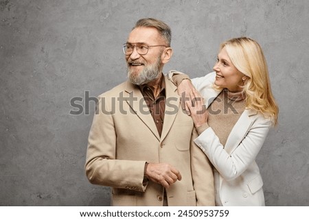A mature, elegant man and woman stand side by side in debonair attire, exuding love and sophistication against a gray backdrop. Royalty-Free Stock Photo #2450953759