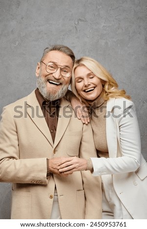 An elegant, mature, loving couple in debonair attire, standing next to each other against a gray backdrop. Royalty-Free Stock Photo #2450953761
