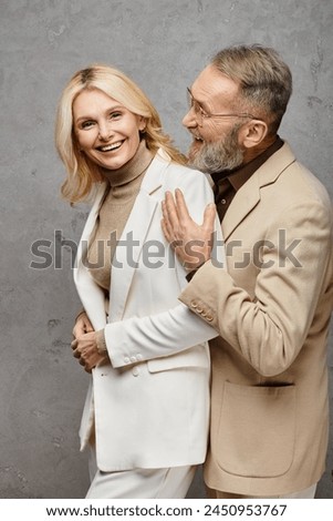 Mature loving couple in debonair attires stand gracefully together against a gray backdrop. Royalty-Free Stock Photo #2450953767
