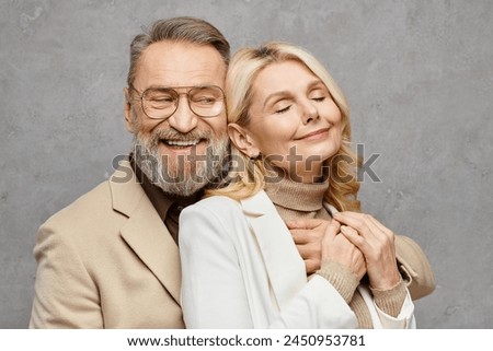 Elegant, mature, loving couple poses in debonair attire against a gray backdrop. Royalty-Free Stock Photo #2450953781