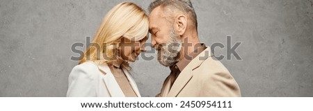 An elegant, mature man and woman in debonair attire stand together against a gray backdrop. Royalty-Free Stock Photo #2450954111