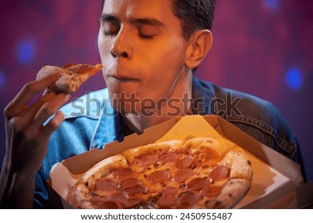 A young guy student eating pizza with pleasure from a cardboard box in a club