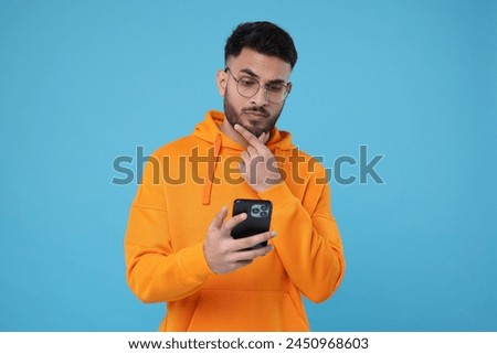 Handsome young man using smartphone on light blue background