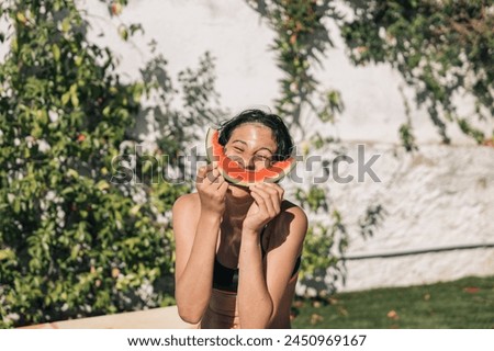 Hispanic girl making the big smile gesture with a slice of watermelon over her mouth, refreshing summer weather.