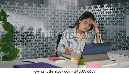 Indian young adult stress business worker woman sitting on chair hold pen writing project work book at indoor job office. Teen girl modern employee do overwork feel tired headache at company workplace