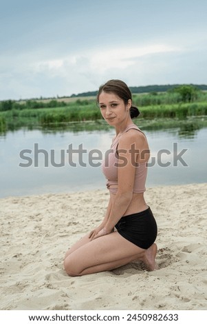 Pretty slim woman in sportwear practicing yoga in sand beach lake, outdoor exercise. Morning workout outdoors