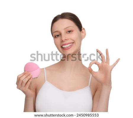Washing face. Young woman with cleansing brush showing OK gesture on white background