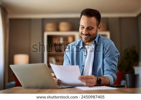 A happy and hopeful young adult man reading and checking his resume before applying for a new job. Royalty-Free Stock Photo #2450987405