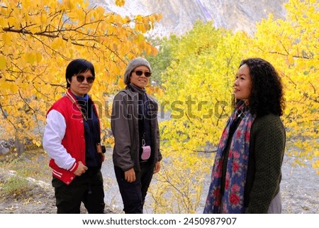 A group of Asian female tourists posing for a picture with a view of the colorful foliage against the tall mountain ranges in the morning light in Passu Valley, Gilgit-Baltistan, Pakistan.