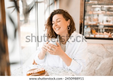 Smiling beautiful blonde woman 28-30 year old drinking coffee with cake in cafe.  Royalty-Free Stock Photo #2450988911